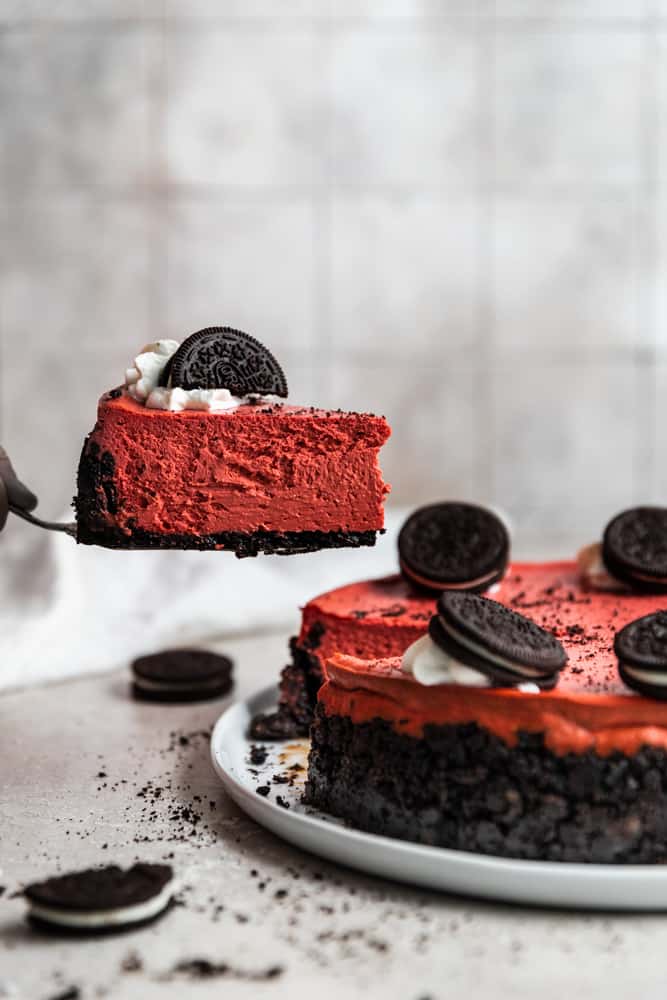 A slice of red velvet cheesecake being picked up by a cake knife.
