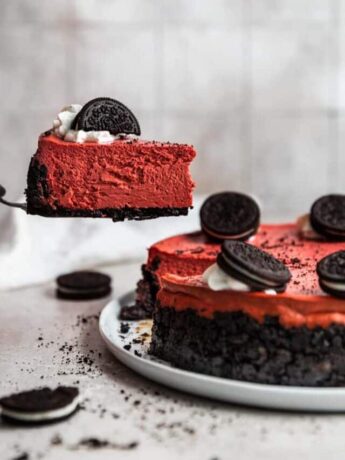 A slice of red velvet cheesecake being picked up by a cake knife.