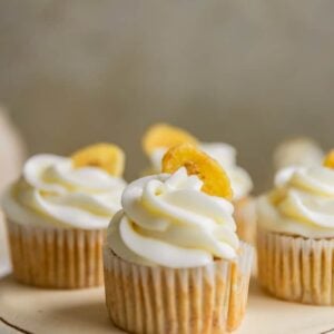 A closeup of a banana cupcake frosted with cream cheese frosting and garnished with a banana chip.