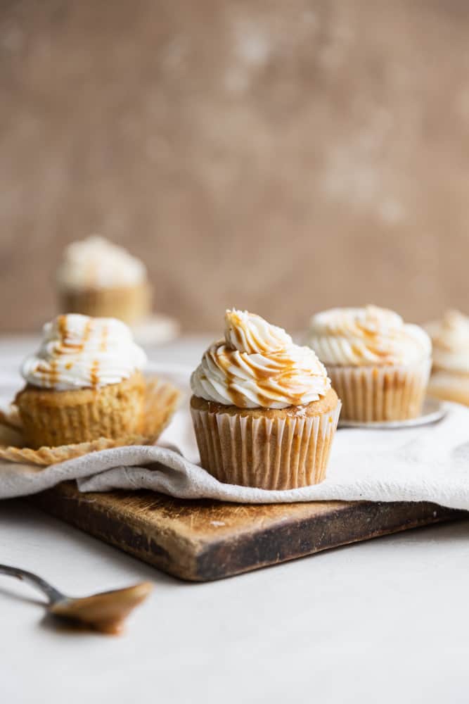 Caramel cupcakes with caramel drizzle on a linen and wooden cutting board.