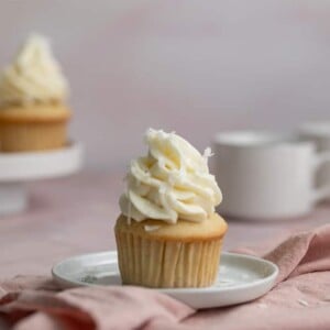 A single coconut cupcake with frosting on a white plate.