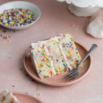 A slice of confetti cake on a pink plate.