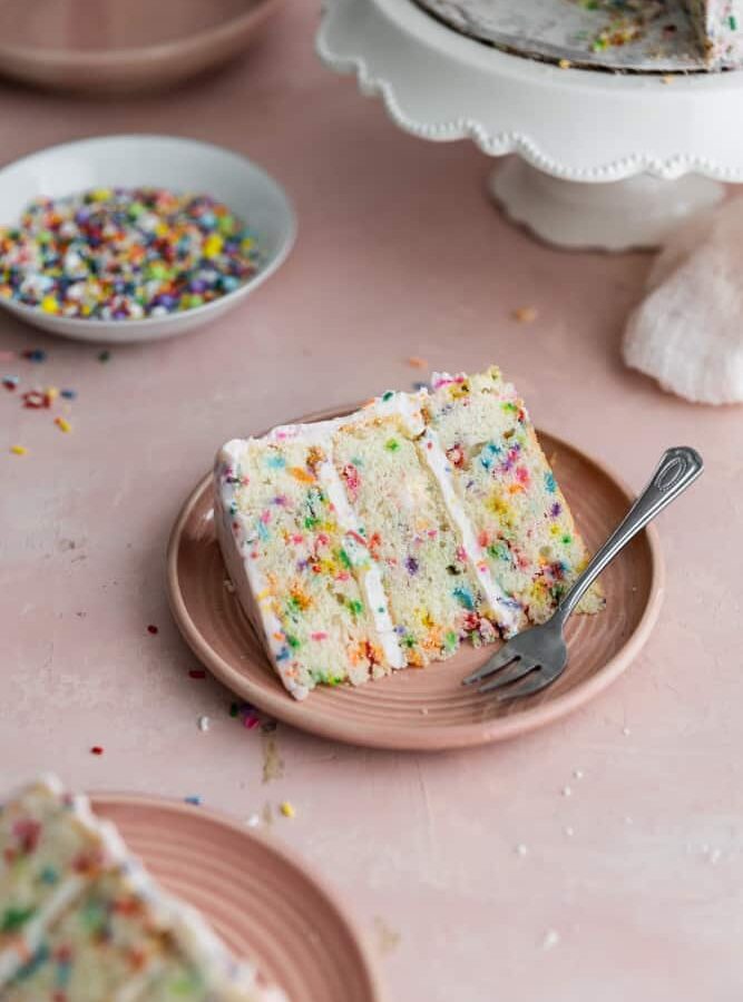 A slice of confetti cake on a pink plate.