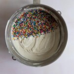 Sprinkles added to vanilla cake batter in a mixing bowl.