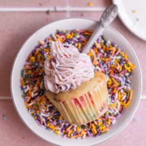 One confetti cupcakes on its side in a bowl of sprinkles.