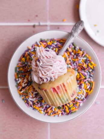 One confetti cupcakes on its side in a bowl of sprinkles.