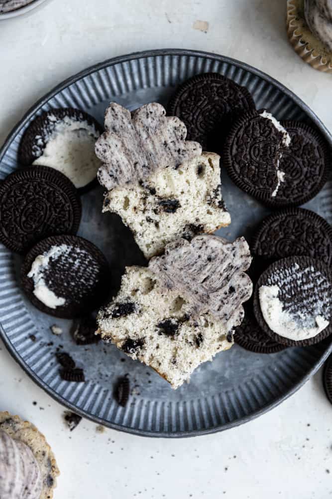 An Oreo cupcake sliced in half on a blue plate next to split open Oreos.