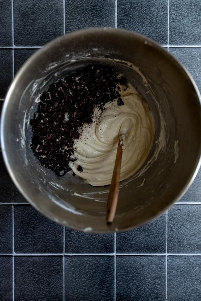 Crushed oreos in vanilla cupcake batter in a bowl.