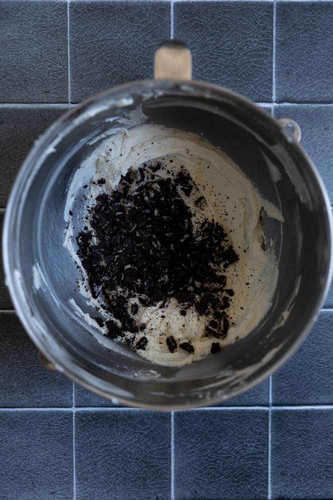 Crushed Oreos on top of vanilla cupcake batter in a mixing bowl.