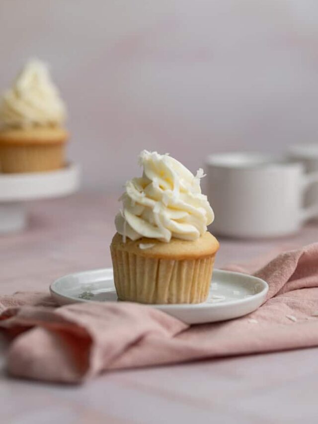 A single coconut cupcake with frosting on a white plate.