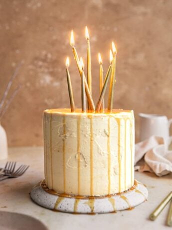 A caramel cake with caramel drizzle and candles on an overturned plate.
