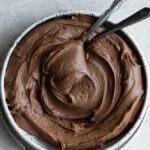 Chocolate cream cheese frosting swirled in a white bowl with 2 spoons.