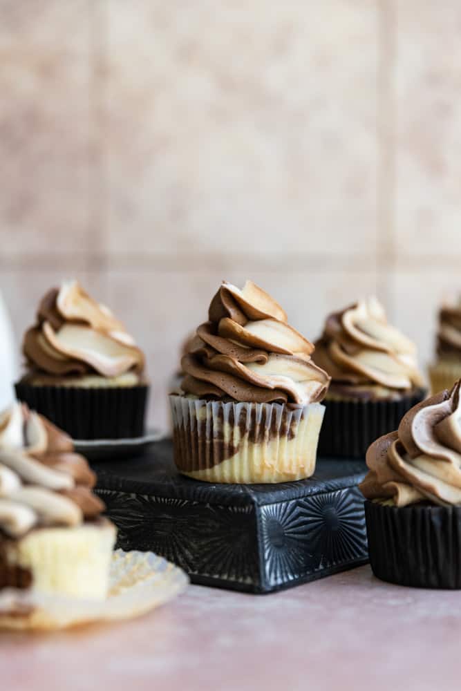 Marble cupcakes with frosting on a black tin stand.