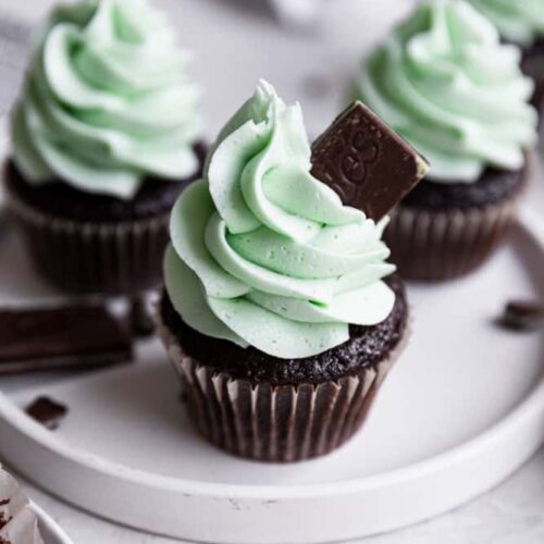 A mint chocolate cupcake on a white plate topped with an Andes mint.