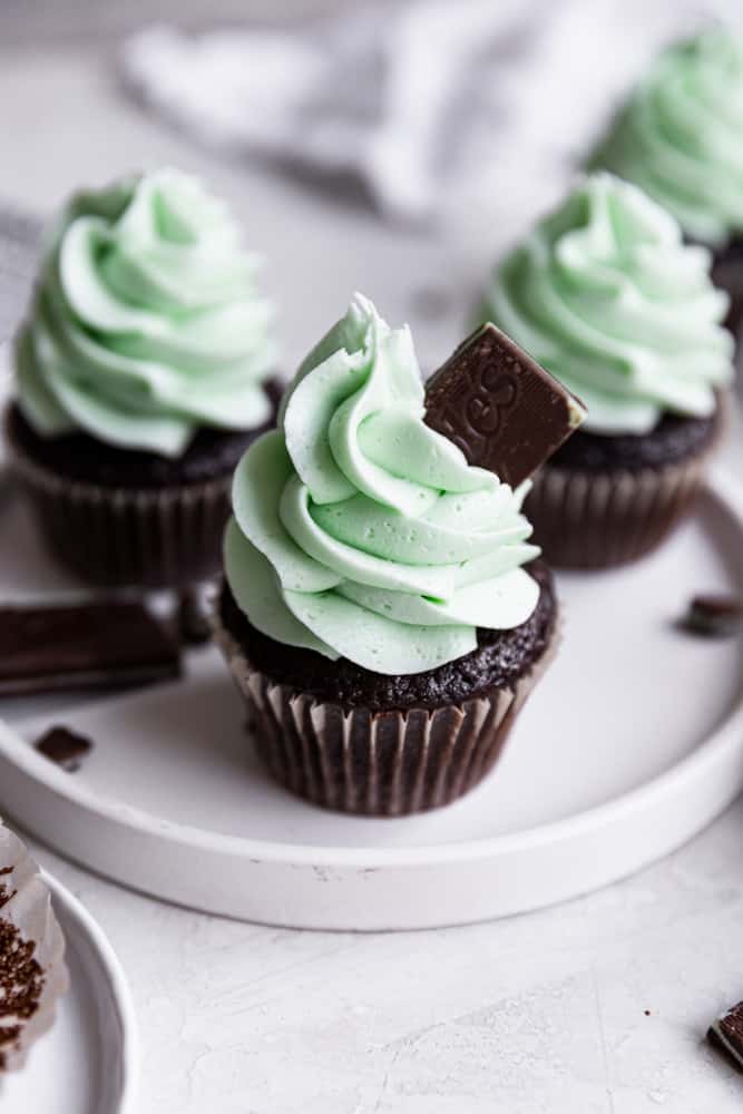 A mint chocolate cupcake on a white plate topped with an Andes mint.