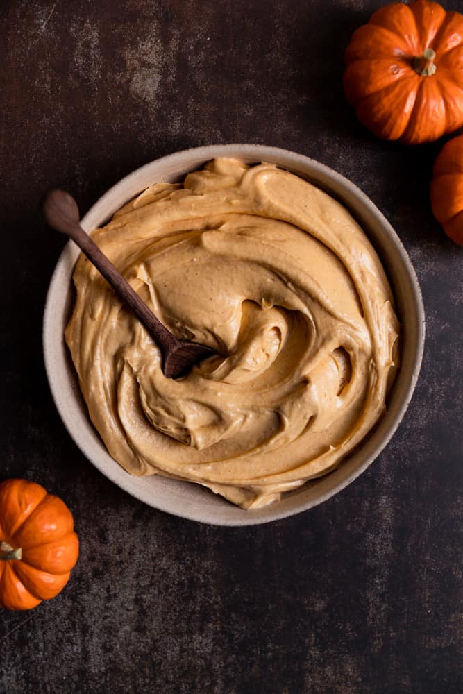 Pumpkin cream cheese frosting in a bowl with a wooden spoon.