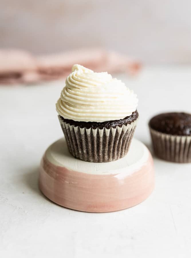 A cupcake on a pink pedestal on a gray surface.