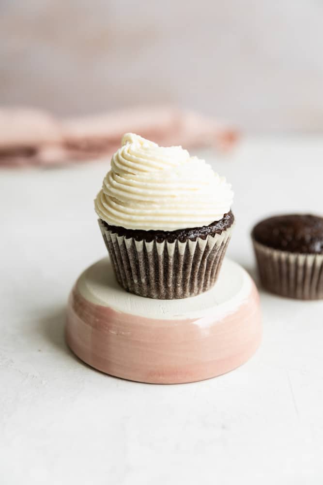 A cupcake on a pink pedestal on a gray surface. 