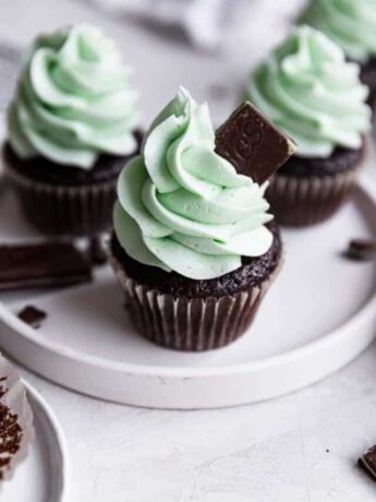 A mint chocolate cupcake on a white plate topped with an Andes mint.