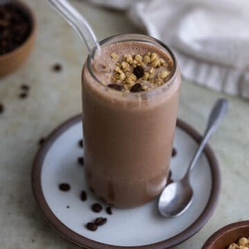 A coffee protein smoothie on a white plate with a straw inside.