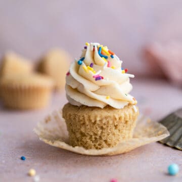 An unwrapped vanilla dairy free cupcake with sprinkles on top.