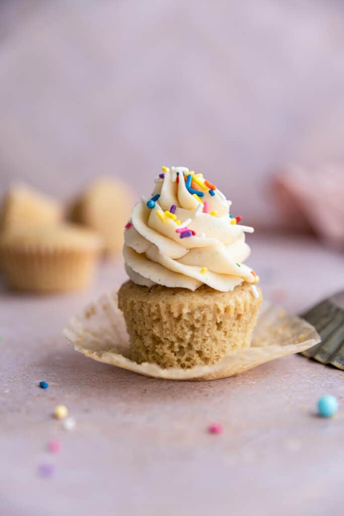 An unwrapped vanilla dairy free cupcake with sprinkles on top.