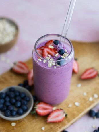 Berries and oats on top of a smoothie in a glass cup.