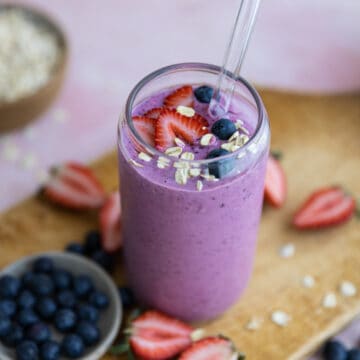 Berries and oats on top of a smoothie in a glass cup.