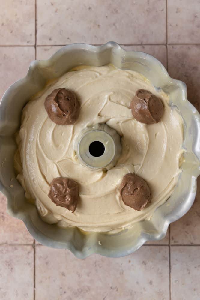 Chocolate batter dolloped over vanilla batter in a bundt pan.