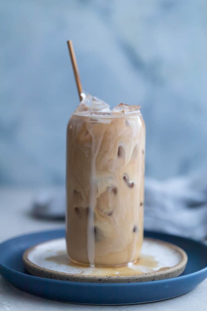 Vanilla iced coffee in a glass cup on a white plate.