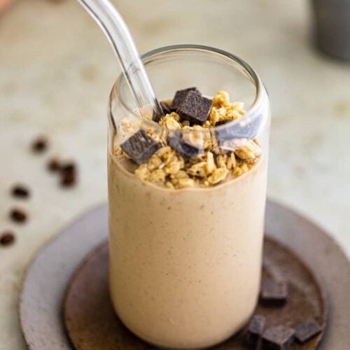 Granola and chocolate on top of a coffee smoothie in a glass cup.