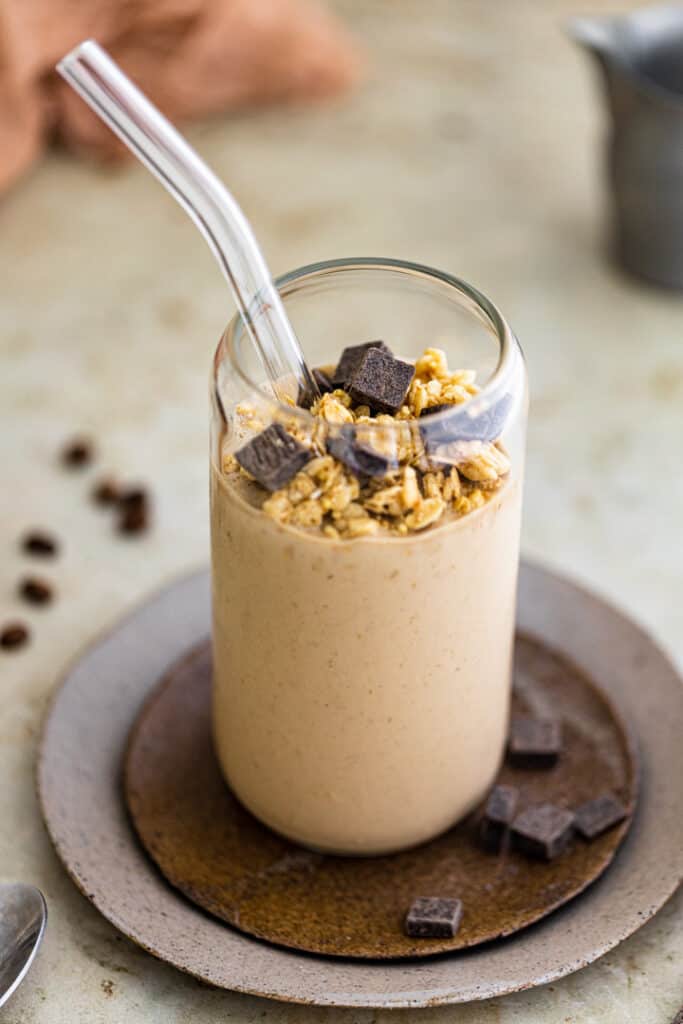 Granola and chocolate on top of a coffee smoothie in a glass cup.