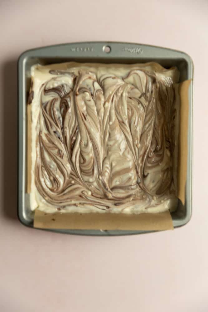 Swirled brownie and cheesecake batter in a pan.