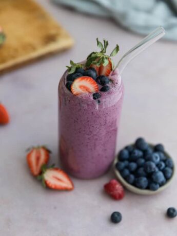 A fruit smoothie in a glass cup topped with strawberries and blueberries.