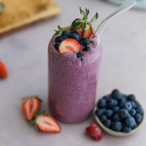 A fruit smoothie in a glass cup topped with strawberries and blueberries.