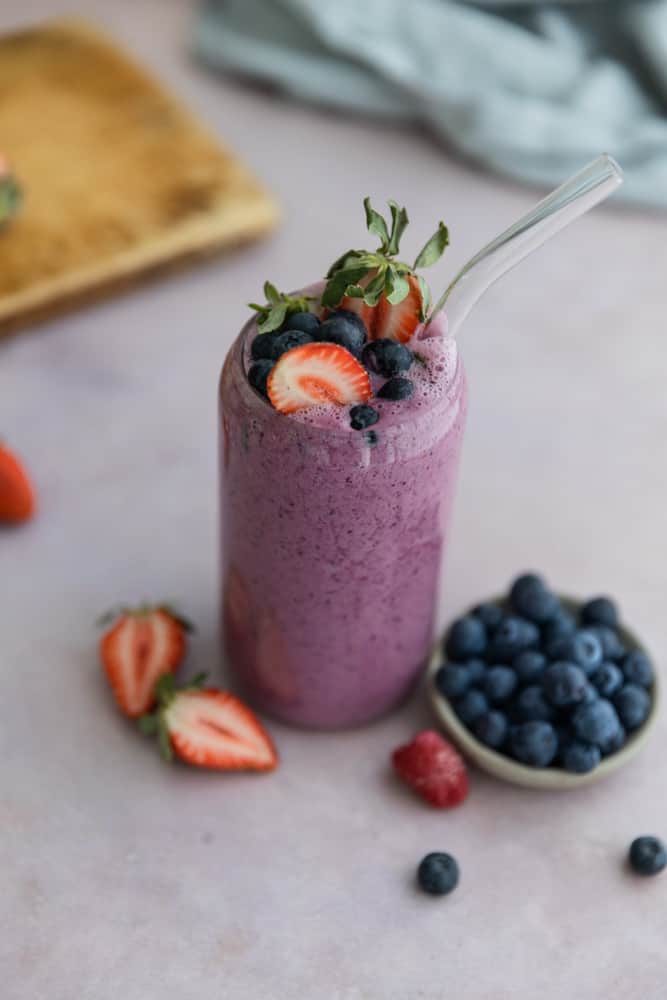 A fruit smoothie in a glass cup topped with strawberries and blueberries. 
