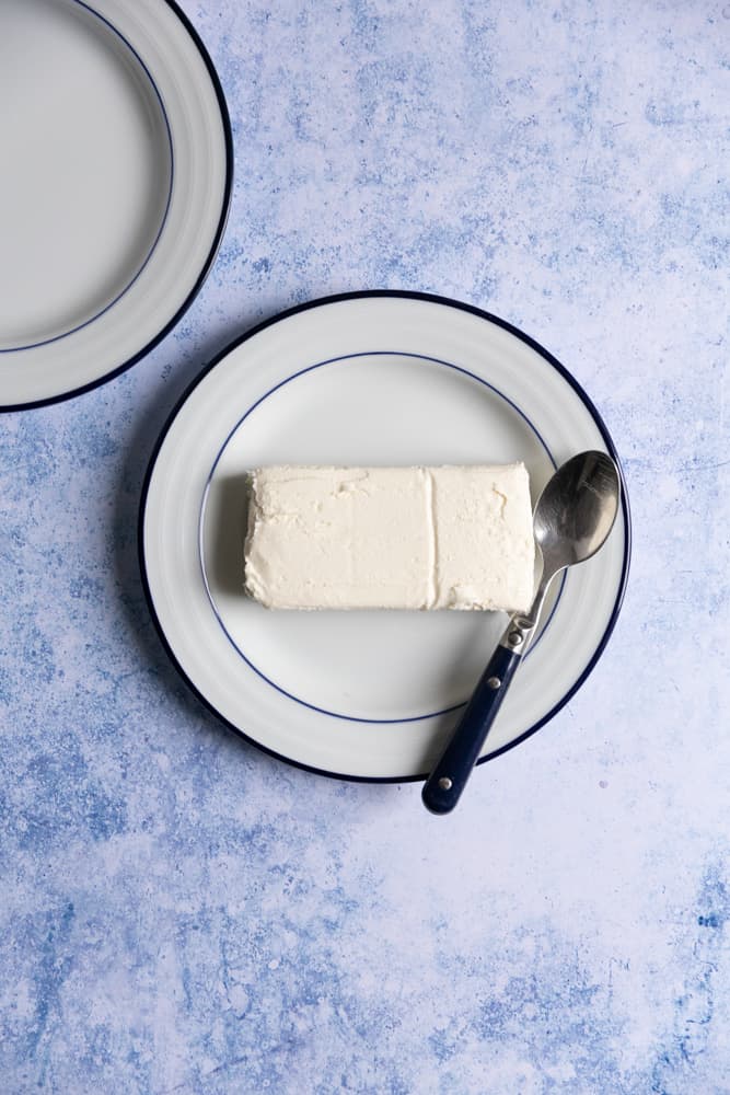 Cold cream cheese on a white plate on a blue background.