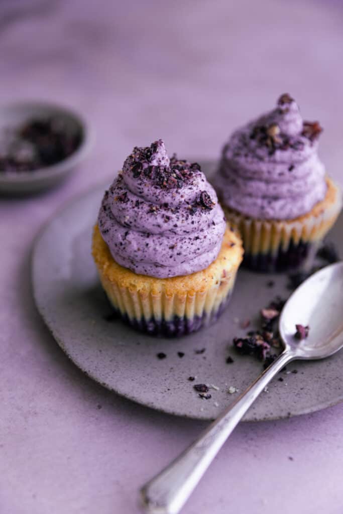 A cupcake on a plate frosted with blueberry frosting.