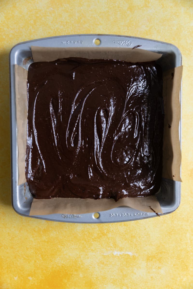 Brownie batter in a 8x8 parchment lined tray.