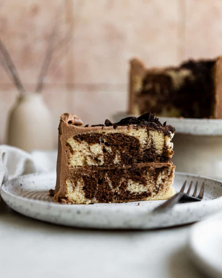 A slice of marble cake standing on a white plate next to a fork.