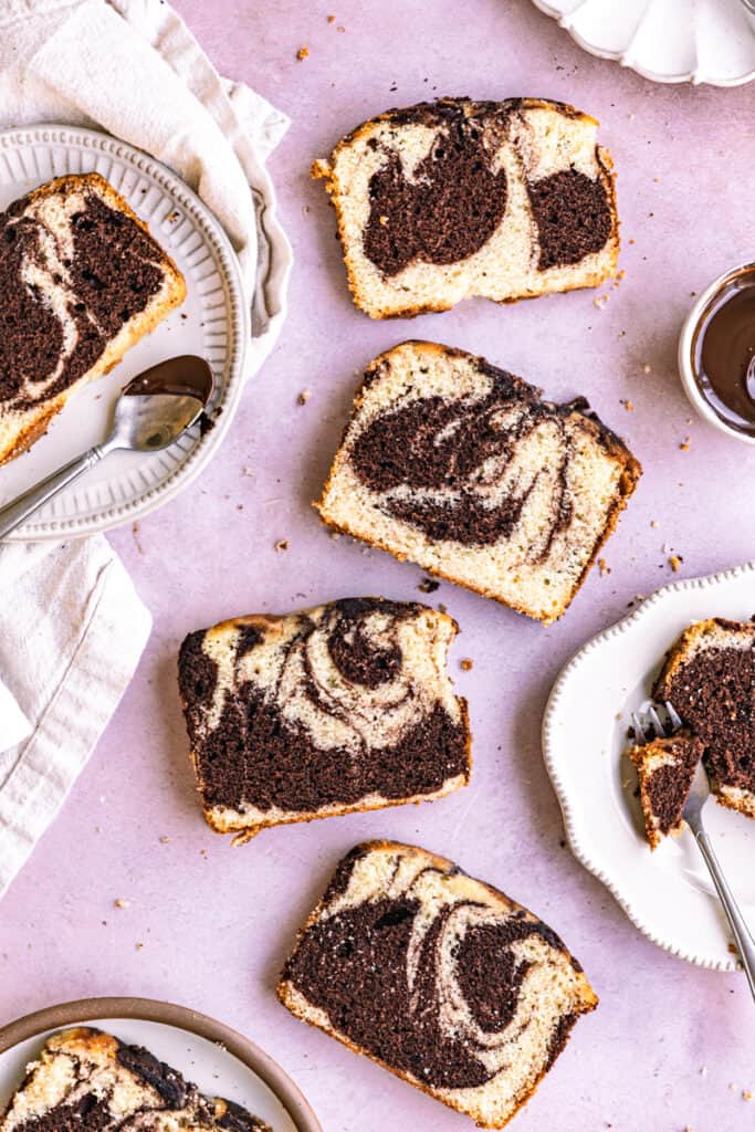 Slices of marble loaf cake on plates next to utensils on a purple surface.