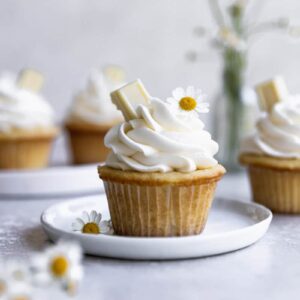 A white chocolate cupcake on a white plate surrounded by white flowers.
