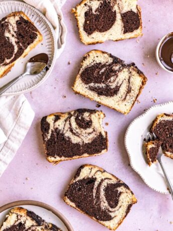 Slices of marble loaf cake on plates next to utensils on a purple surface.