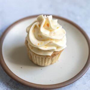 Orange buttercream frosted on top of a vanilla cupcake.