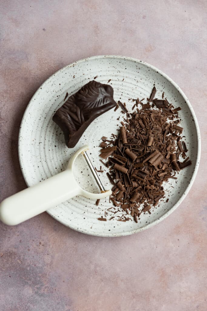 Shaved chocolate next to a peeler on a white plate.