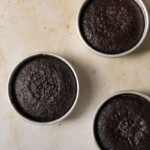 3 chocolate cakes in their pans on a dark beige background.