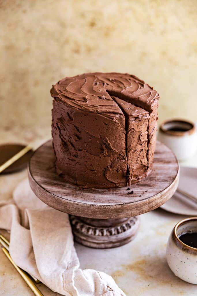 A chocolate coffee cake with a slice cut out on a wooden cake stand.