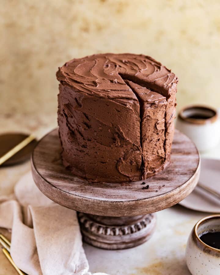 A chocolate coffee cake with a slice cut out on a wooden cake stand.