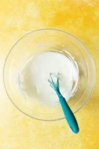 A glaze icing in a glass bowl with a mini spatula inside of it.