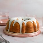 A bundt cake drizzled with thick white frosting on a pink plate.